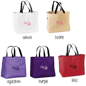 May include: Five Mary Kay tote bags in different colors: white, stone, hyacinth, purple, and red. Each bag has black handles and a Mary Kay logo embroidered on the front.