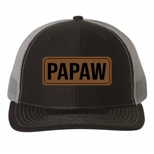 May include: Black and gray trucker hat with a brown patch that says "PAPAW" in black letters.