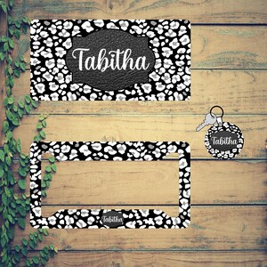 May include: A set of three black and white leopard print car accessories. The set includes a license plate frame, a key chain, and a small rectangle with the name "Tabitha" on it.