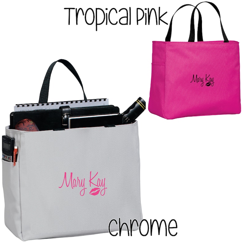 May include: Two Mary Kay tote bags, one in chrome and one in tropical pink. Both bags have black handles and the Mary Kay logo with a pink lip is embroidered on the front.