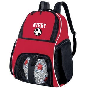 May include: Red and black soccer backpack with a white soccer ball graphic and the name Avery printed on the front. The backpack has a mesh pocket on the front for a soccer ball.