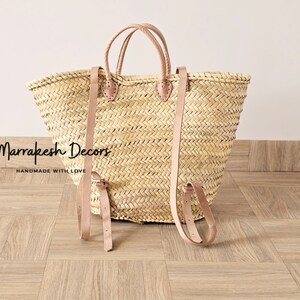 May include: A large, natural woven straw tote bag with leather straps and handles. The bag has a  "Marrakesh Decors" label and the text "Handmade with Love".