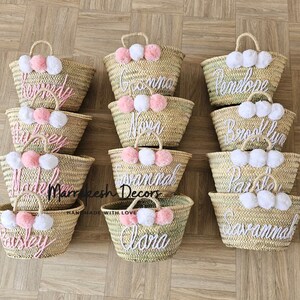 May include: Ten straw tote bags with pom poms and personalized names in pink and white thread. The names are: Kennedy, Grandma, Penelope, Brooklyn, Paisley, Madeline, Savannah, Paris, Alana, Savannah.