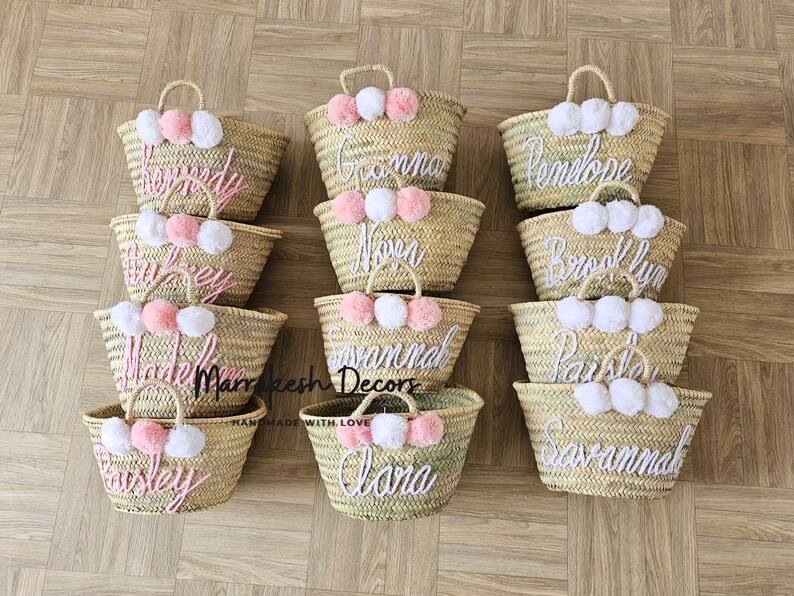 May include: Ten straw tote bags with pom poms and personalized names in pink and white thread. The names are: Kennedy, Grandma, Penelope, Brooklyn, Paisley, Madeline, Savannah, Paris, Alana, Savannah.