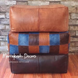 May include: Three leather ottomans stacked on top of each other. The top ottoman is a solid tan color, the middle one has a patchwork design of denim and brown squares, and the bottom one is dark brown. The text "Marrakesh Decors Handmade With Love" is visible.