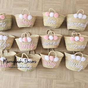 May include: Ten straw tote bags with pom poms and personalized names in white embroidery. The names are:  Dona, Aubrey, Nova, Savannah, Brooklyn, Kennedy, Savannah, Grandma, Madeline, and Paisley. The bags are handmade with love by Marrakesh Decors.