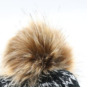 Puede incluir: Gorro de punto negro y blanco con un pomp&oacute;n marr&oacute;n esponjoso.