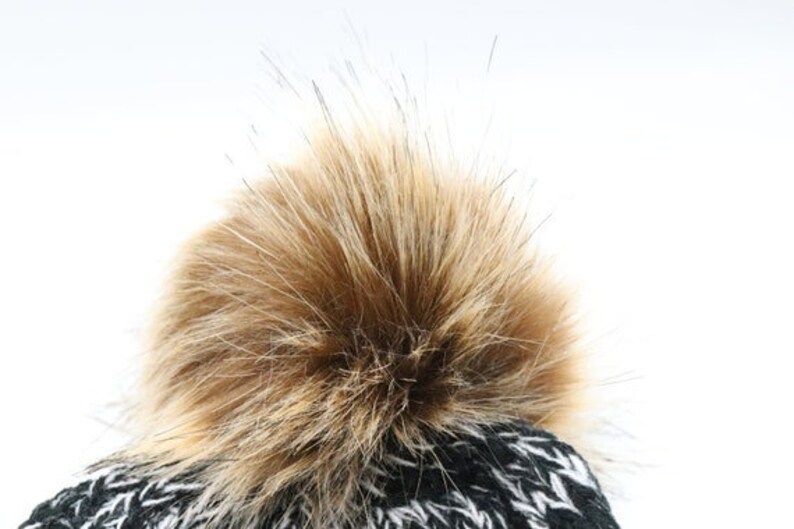 Puede incluir: Gorro de punto negro y blanco con un pomp&oacute;n marr&oacute;n esponjoso.