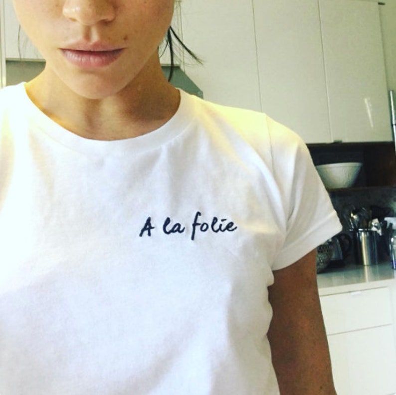 May include: White t-shirt with the French phrase "A la folie" embroidered in black on the front.