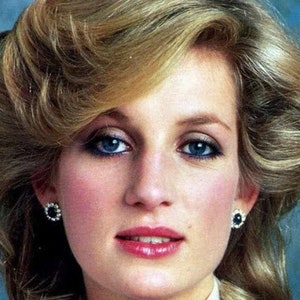 May include: A woman with blonde hair styled in a bouffant, wearing a white collared shirt and earrings. Her makeup features blue eyeshadow and a light pink lipstick.