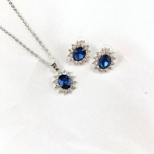 May include: A silver necklace and earrings set with a large blue oval gemstone surrounded by smaller clear stones.