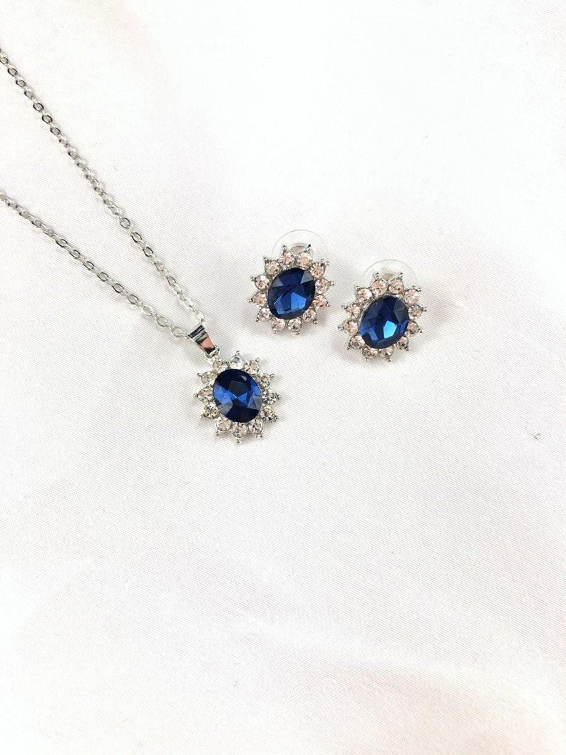 May include: A silver necklace and earrings set with a large blue oval gemstone surrounded by smaller clear stones.