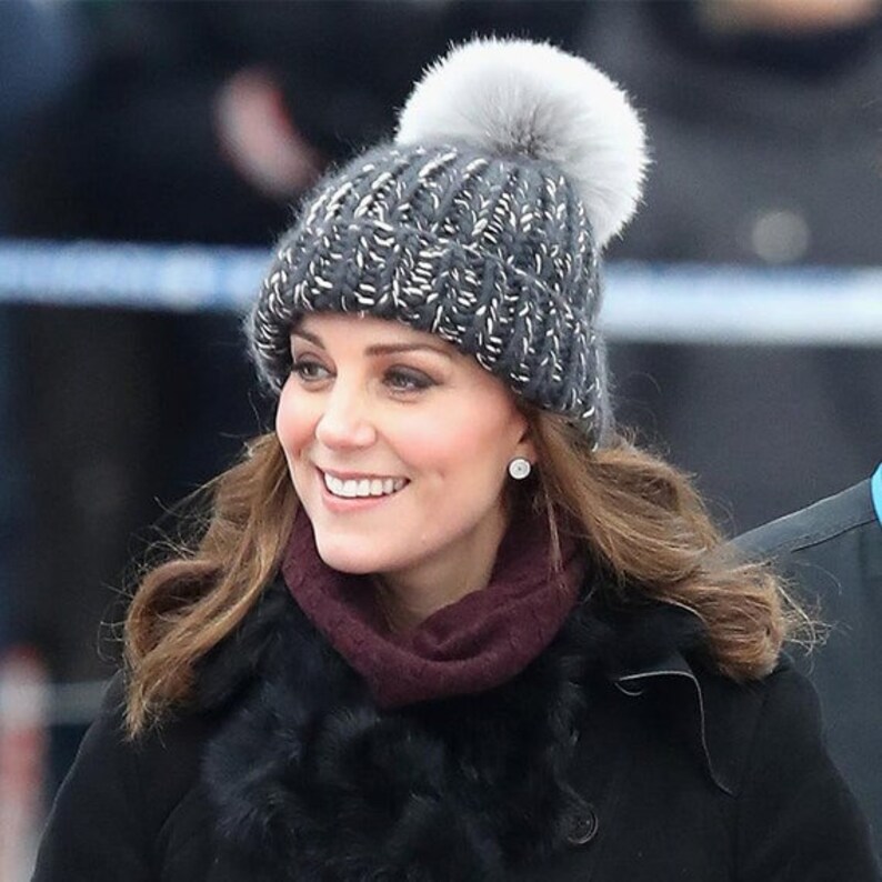 Puede incluir: Una mujer con un gorro de punto gris con un pomp&oacute;n blanco y una bufanda de piel negra. Est&aacute; sonriendo y mirando hacia la derecha.