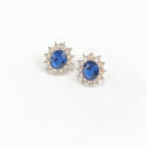 May include: A pair of silver stud earrings with a large blue oval-shaped gemstone surrounded by smaller clear gemstones.
