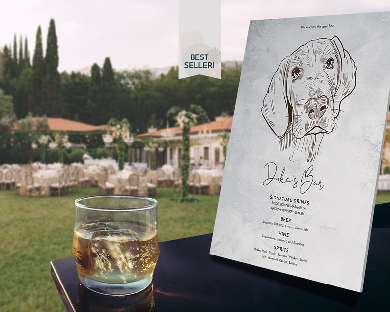 May include: A sign for "Duke's Bar" featuring a dog illustration, with a list of signature drinks, beer, wine, and spirits. A glass of amber liquid with ice sits in front of the sign. The sign has a "Best Seller!" sticker.