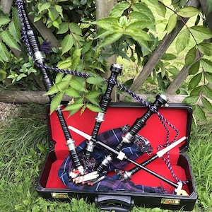 Puede incluir: Un conjunto de gaitas negras con una funda de transporte negra y un forro de tela tartán. Las gaitas están en una funda con un interior rojo.