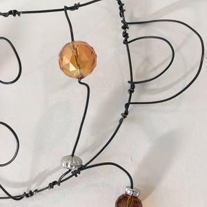 May include: A wire sculpture with two amber glass beads and a silver bead. The wire is twisted and shaped into a design that resembles a cup.