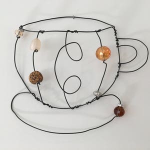 May include: A wire sculpture of a coffee cup with a saucer, decorated with brown, beige, and orange beads.