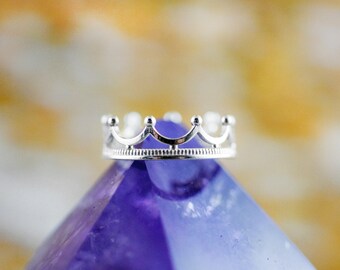 Könnte beinhalten: Ein silberner Kronenring mit einem filigranen Design, der auf einem violetten Amethystkristall liegt.