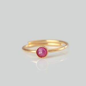 Könnte beinhalten: Ein goldener Ring mit einem einzigen, runden, rosafarbenen Edelstein in der Mitte.