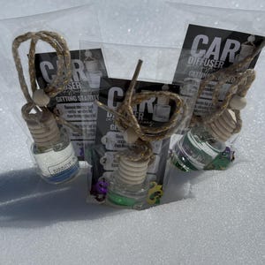 May include: Three car air fresheners in clear glass bottles with gold string and wooden beads. The bottles are labelled "BIBBIDE" and "CAR DIFFUSER GETTING STARTED".