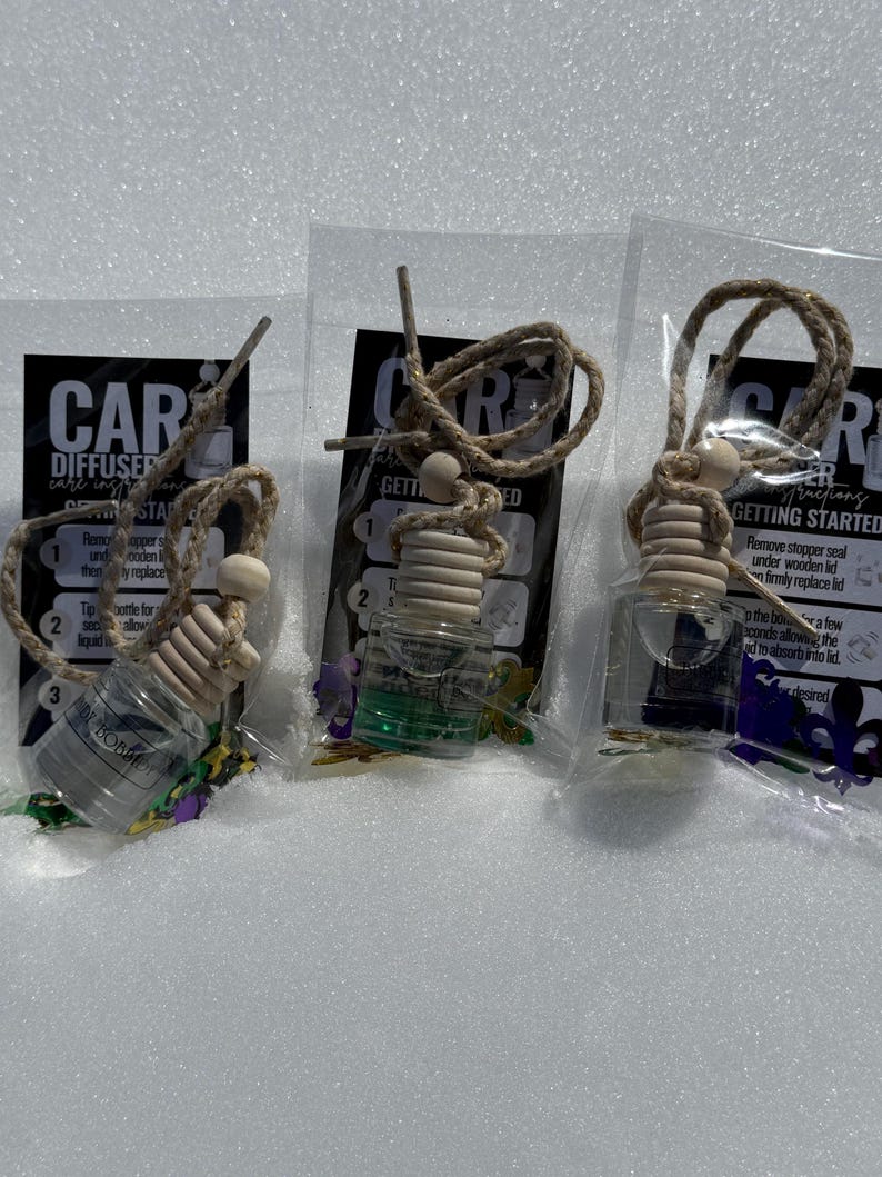Puede incluir: Tres ambientadores de coche en botellas de vidrio transparente con una mecha de madera y una cuerda dorada. Las botellas est&aacute;n llenas de un l&iacute;quido verde y tienen un dise&ntilde;o tem&aacute;tico de Mardi Gras en dorado y morado. Las instrucciones para usar los ambientadores est&aacute;n impresas en el embalaje.