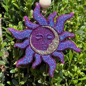 May include: Purple and gold glitter sun and moon ornament with a white wooden bead at the top.