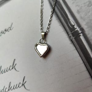May include: A silver heart-shaped pendant necklace with a reflective surface. The necklace is on a white surface.