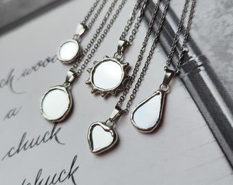 May include: Five silver-toned necklaces featuring small mirror pendants in various shapes, including circular, sunburst, and heart designs. Each pendant is suspended from a matching silver-toned chain, showcasing reflective surfaces and metallic frames.