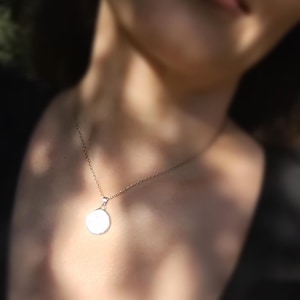 May include: A silver necklace with a round pendant. The pendant is smooth and white.