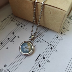 May include: A silver chain necklace with a round pendant featuring a white flower pressed inside clear resin.