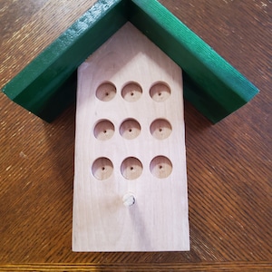 May include: A wooden bee house with a green roof. The house has 16 holes for bees to nest in.