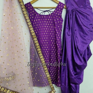 Op de afbeelding: Een paarse en gouden salwar kameez set met een doorschijnende dupatta. De kameez heeft een ronde halslijn en een mouwloos ontwerp. De salwar is een broek met een dhoti-stijl. De dupatta is een doorschijnende sjaal met een gouden rand.