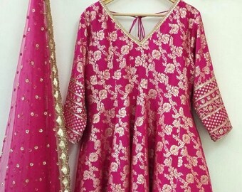 May include: A pink and gold brocade dress with a matching sheer dupatta. The dress has a V-neckline and 3/4 sleeves. The dupatta has a gold border and sequins.