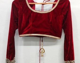 May include: A red velvet blouse with long sleeves and gold trim. The blouse has a tie at the back and gold embellishments on the sleeves.
