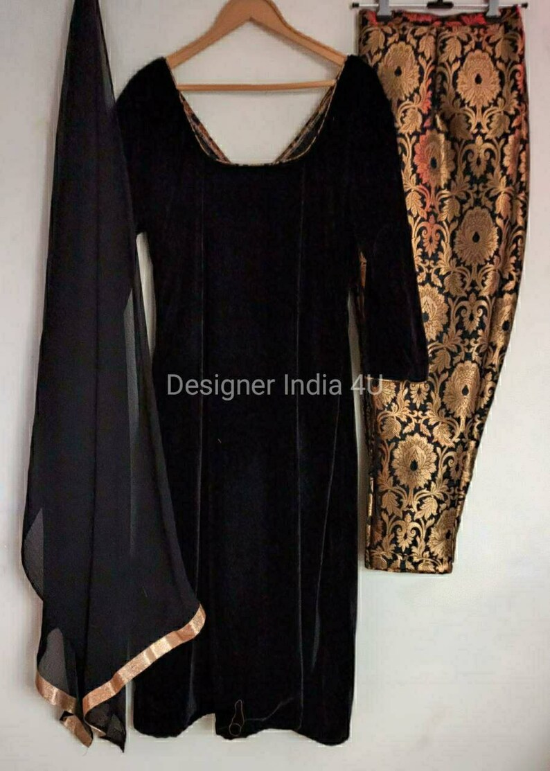 Puede incluir: Una kurta de terciopelo negro con mangas largas y cuello redondo. La kurta se combina con pantalones negros con un estampado floral dorado y negro. Se incluye una dupatta negra transparente con ribete dorado.