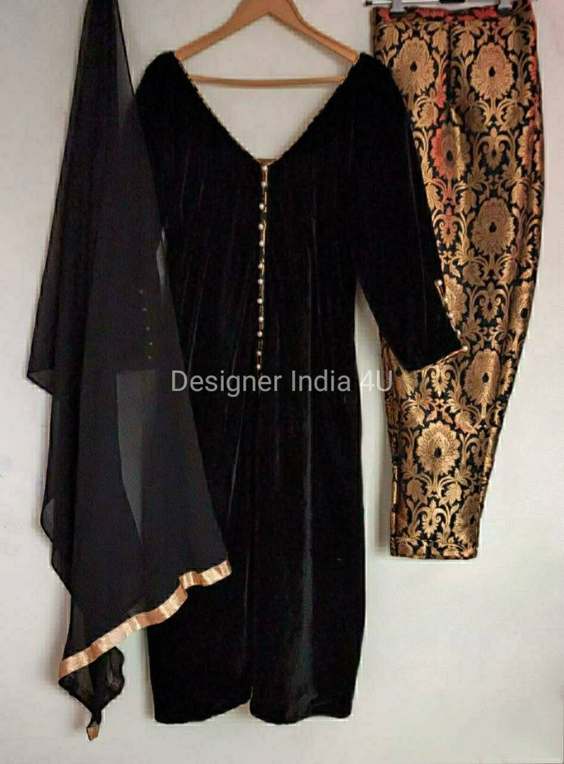 Puede incluir: Una kurta de terciopelo negro con escote en V y detalles de botones de perla. La kurta se combina con pantalones de brocado negro y dorado y una dupatta negra transparente.