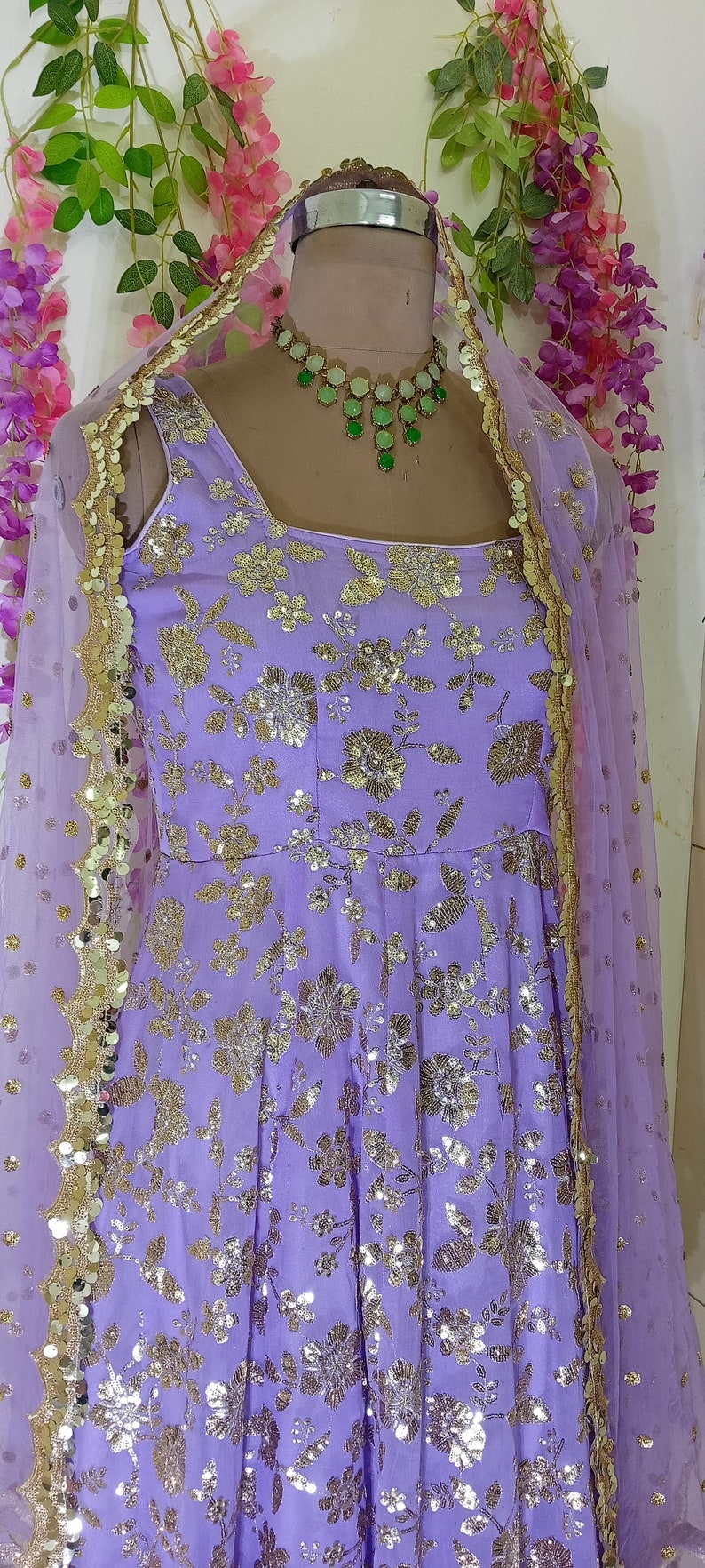 May include: A lavender-colored dress with gold floral embroidery and sequins. The dress has a sleeveless design and a sheer dupatta with gold trim.