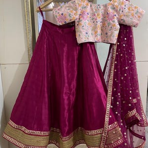 Puede incluir: Una falda magenta con ribete dorado, una blusa bordada rosa con dise&ntilde;os florales y un dupatta de red magenta con lentejuelas doradas.