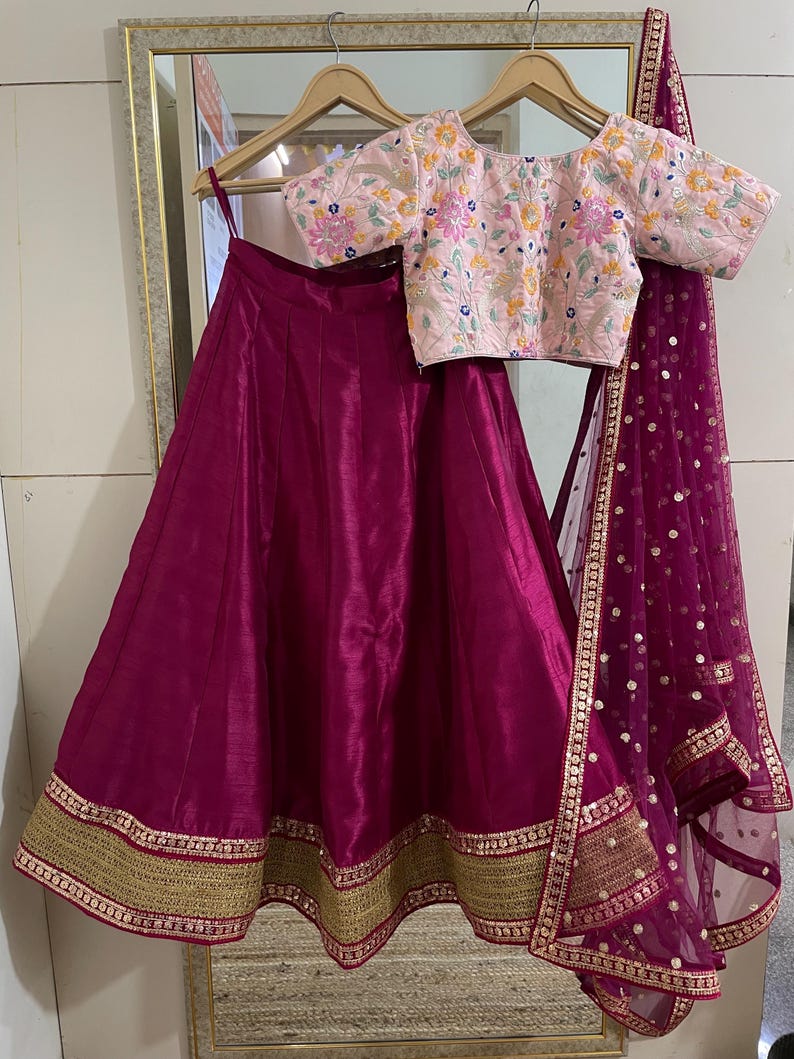 Puede incluir: Una falda magenta con ribete dorado, una blusa bordada rosa con dise&ntilde;os florales y un dupatta de red magenta con lentejuelas doradas.
