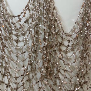 May include: A shimmering, draped accessory featuring a delicate net of interconnected strands. Each strand is adorned with small, reflective, circular embellishments, creating a cascade of light and texture. The color is a soft, warm brown.