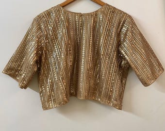 May include: A gold sequined crop top with short sleeves. The top has a vertical striped pattern.