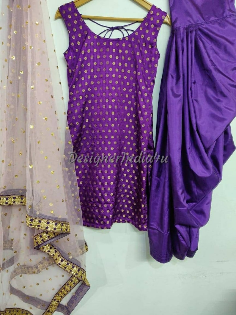 Op de afbeelding: Een paars en gouden geprint, mouwloos top met een bijpassende paarse dhoti rok en een doorschijnende paarse dupatta met gouden pailletten en een gouden en paarse rand.