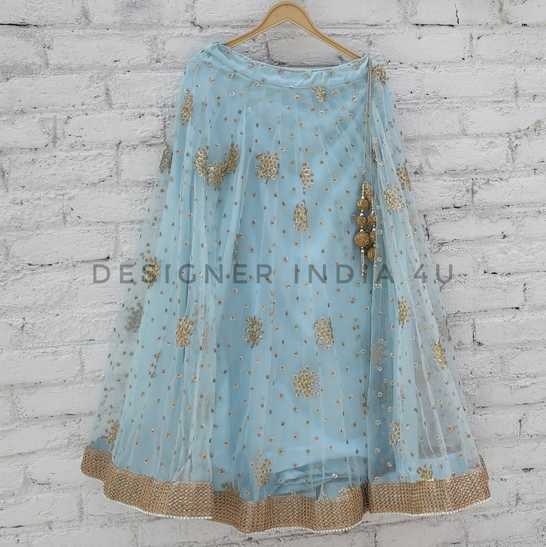 May include: A light blue skirt with gold embroidery and a gold tassel. The skirt is made of a sheer fabric and has a flowing silhouette.
