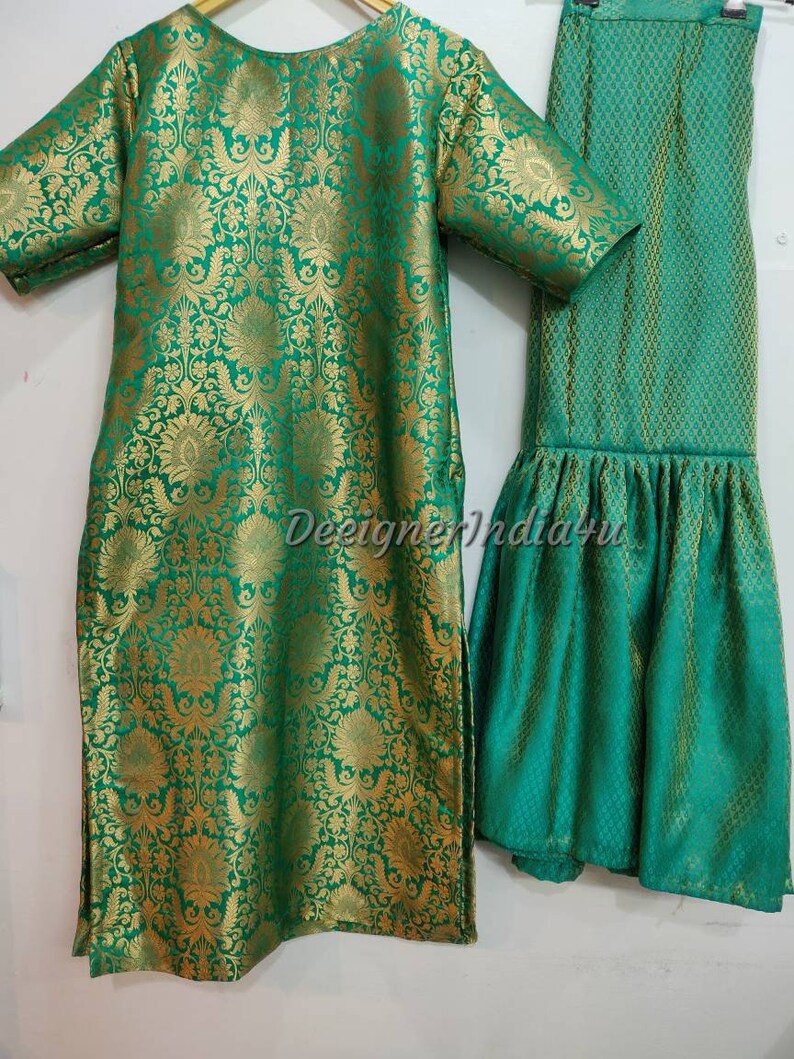 May include: A two-piece green and gold brocade outfit. The top is a tunic with short sleeves and a round neckline. The matching pants have a flared hem. The fabric has a floral pattern.
