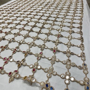 May include: A large, rectangular textile with a grid-like pattern. The grid is made of gold-colored thread, and each intersection features a small, round mirror. The mirrors reflect light and have colorful accents.