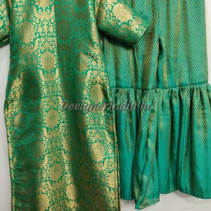 May include: A two-piece green and gold brocade outfit. The top is a long tunic with short sleeves, and the matching bottoms are a skirt with a ruffled hem. The fabric has a floral pattern.