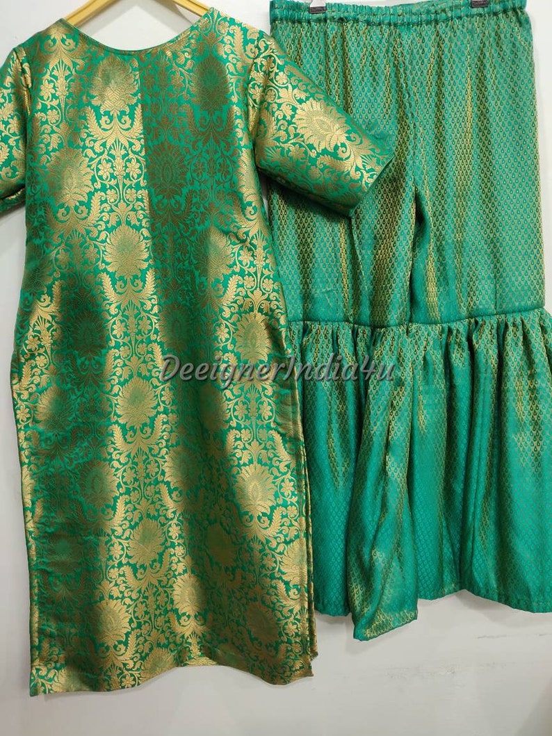 May include: A two-piece green and gold brocade outfit. The top is a long tunic with short sleeves, and the matching bottoms are a skirt with a ruffled hem. The fabric has a floral pattern.