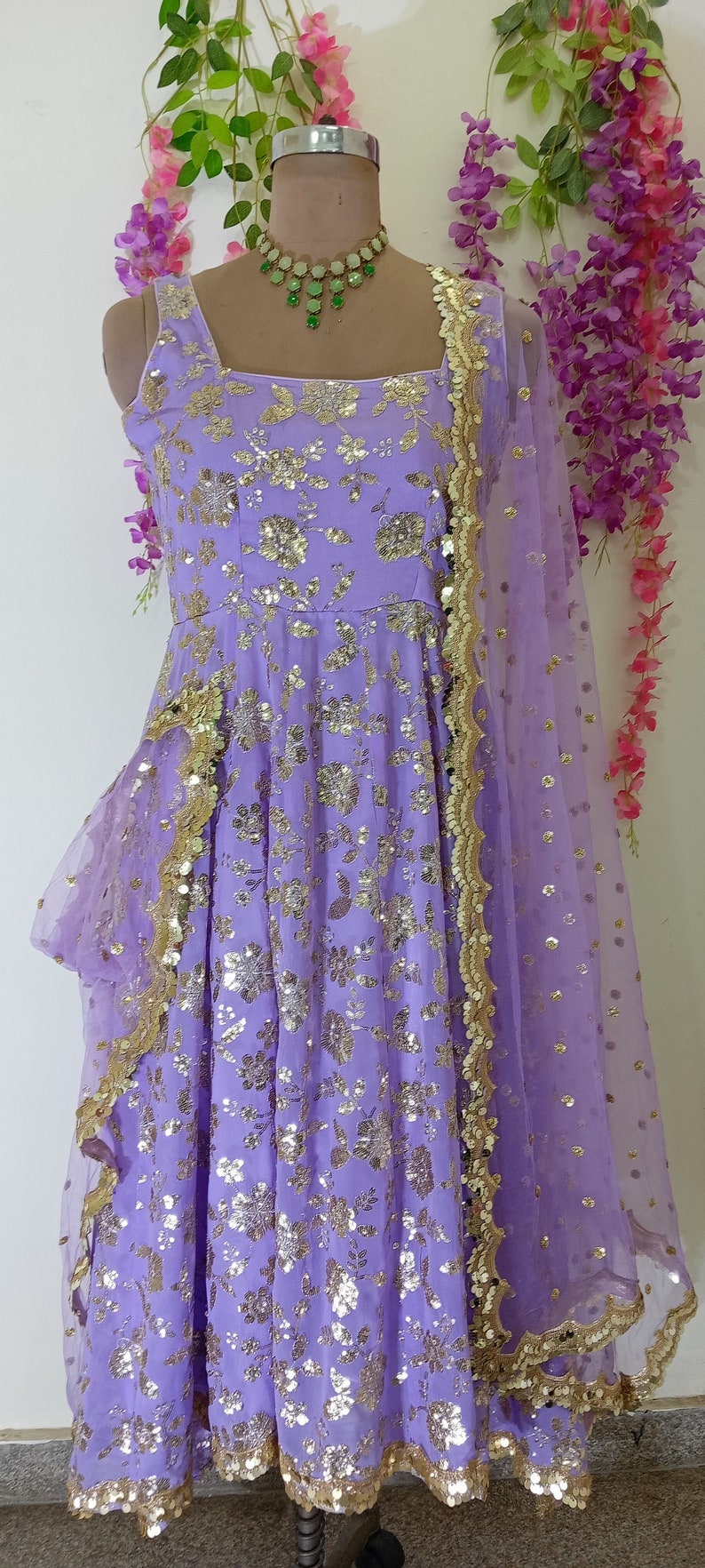 May include: A lavender-colored dress with gold sequins and floral embroidery. The dress has a ruffled hem and a matching sheer dupatta with a gold border.