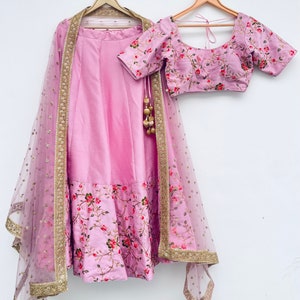 May include: A pink and gold Indian bridal outfit with a floral print. The outfit includes a skirt, a blouse, and a sheer dupatta with gold embroidery.